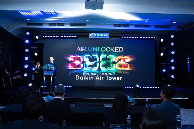 A person standing on a stage with a large screenDescription automatically generated